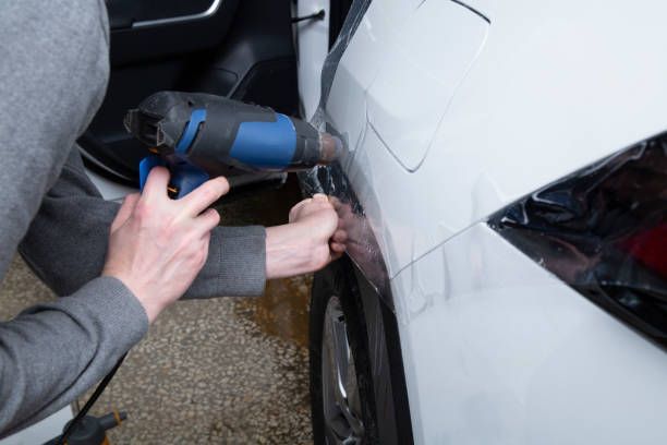 A man is applying a protective film to the side of a white car.