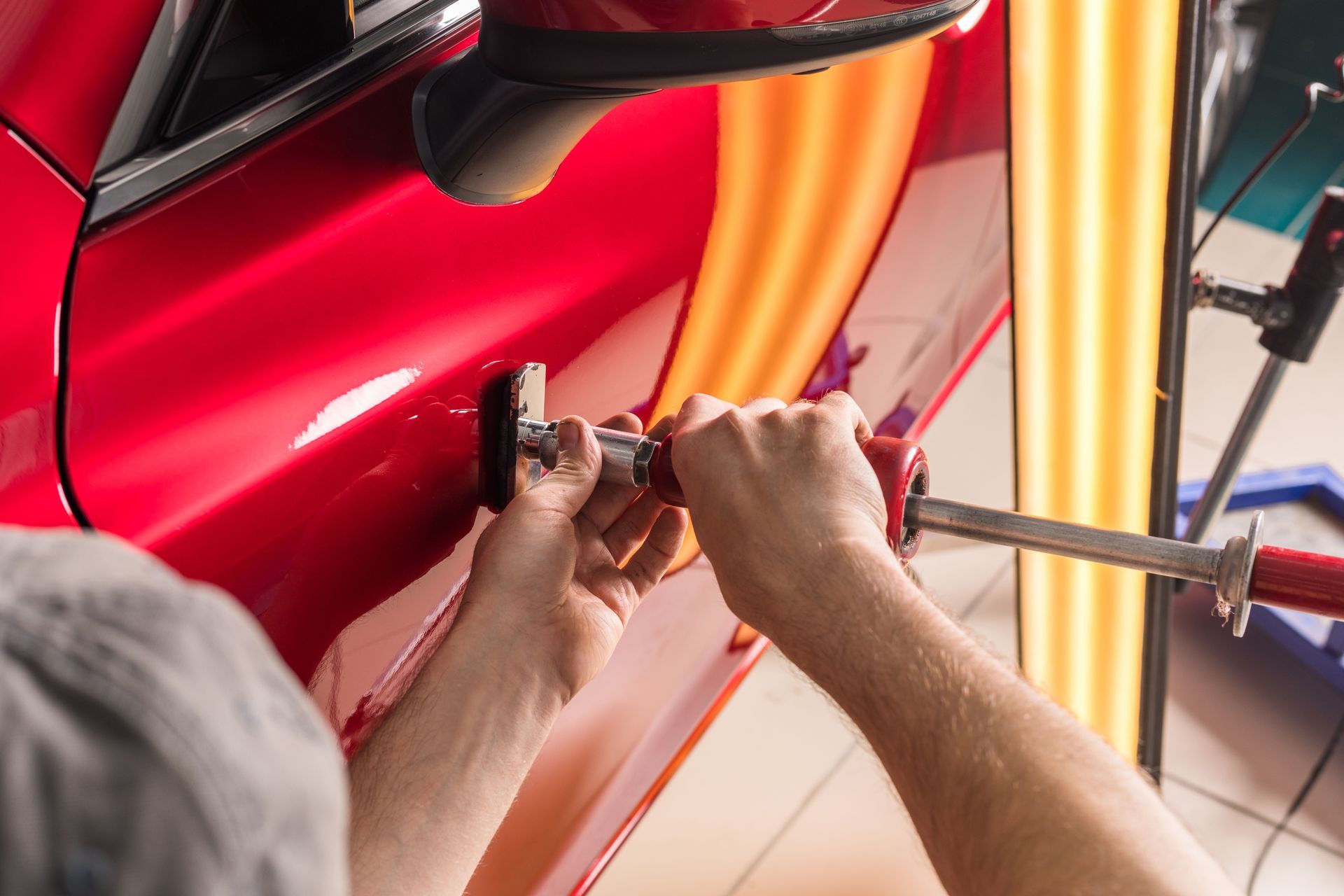 A man is working on a red car door with a wrench.