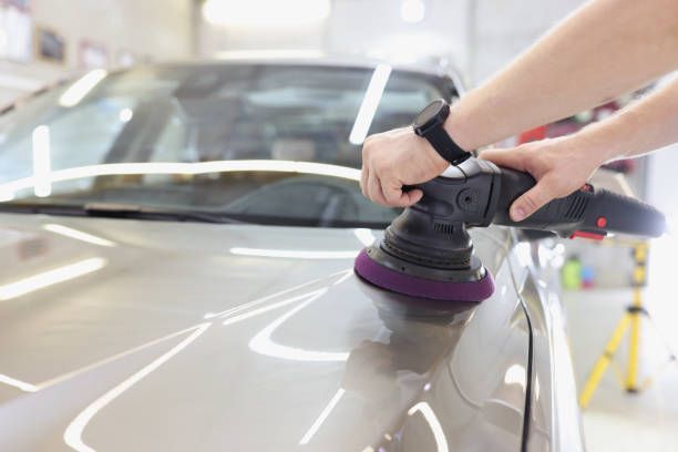 A person is polishing the hood of a car with a machine.