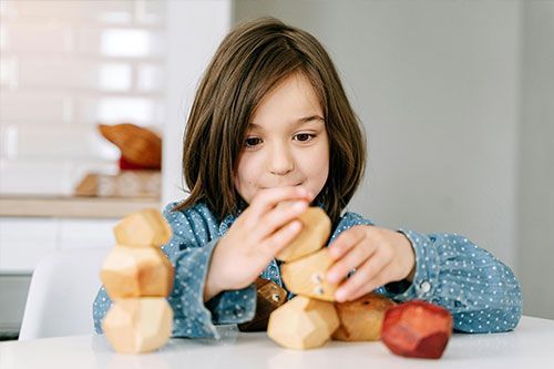 Child stacking wooden toy blocks on a white table indoors