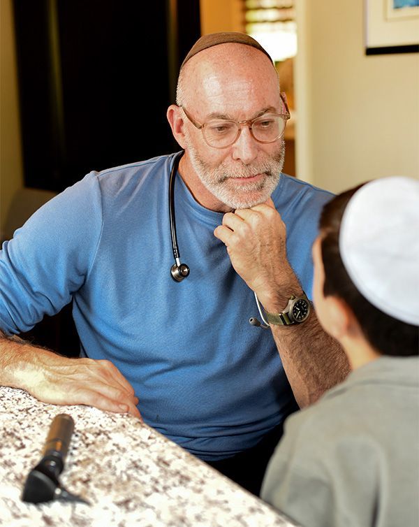 Doctor with stethoscope consults with patient, both wearing religious head coverings, at a countertop.