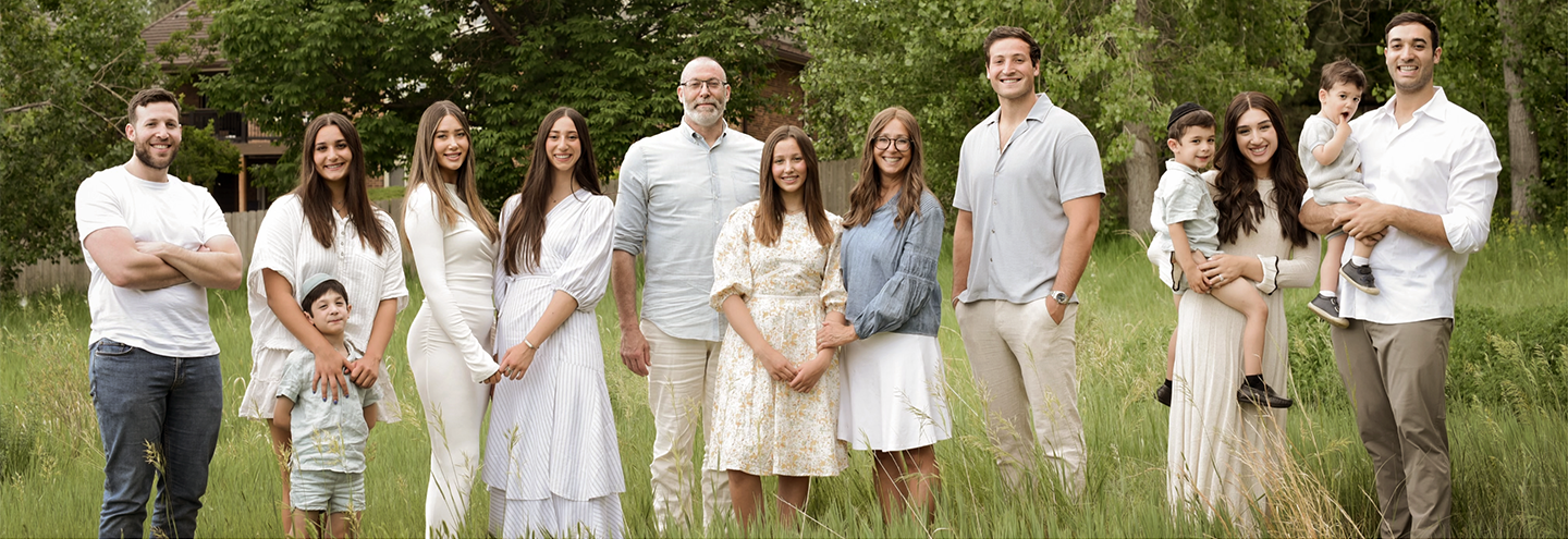 Large family posing outdoors; white and light-colored clothing; grass and trees background.