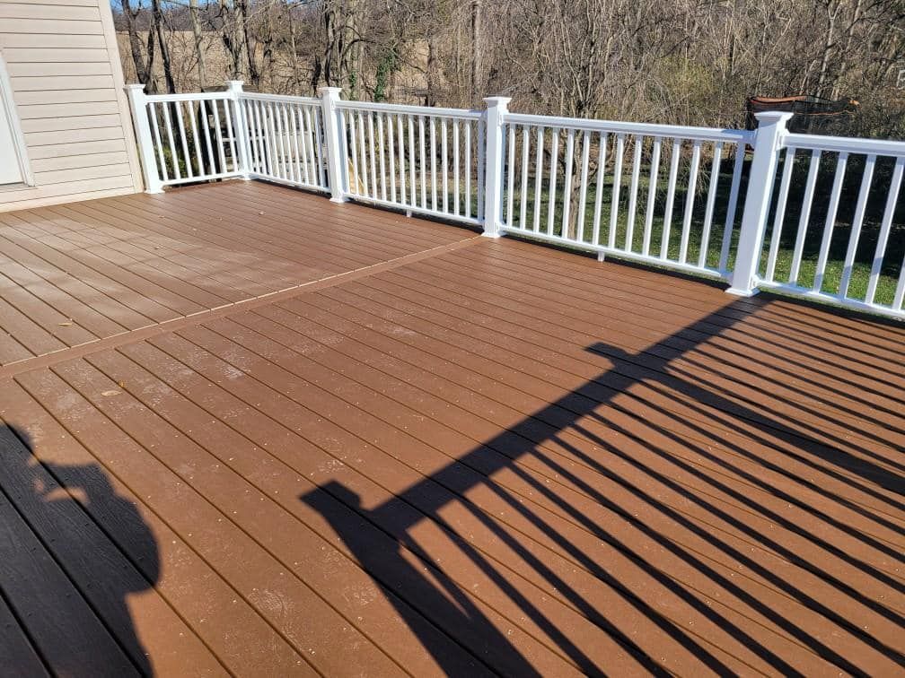 Brown composite deck with white railing, casting long shadow outdoors.