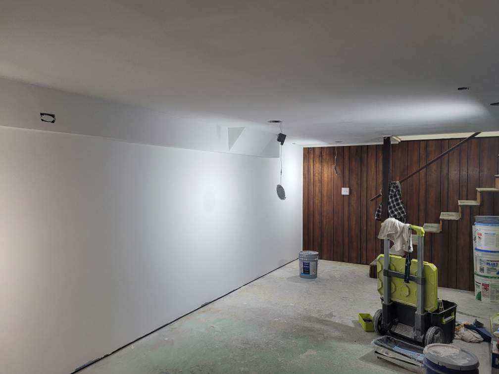Renovated basement interior: white walls, wood paneling, and unfinished flooring. Tools and materials scattered around.