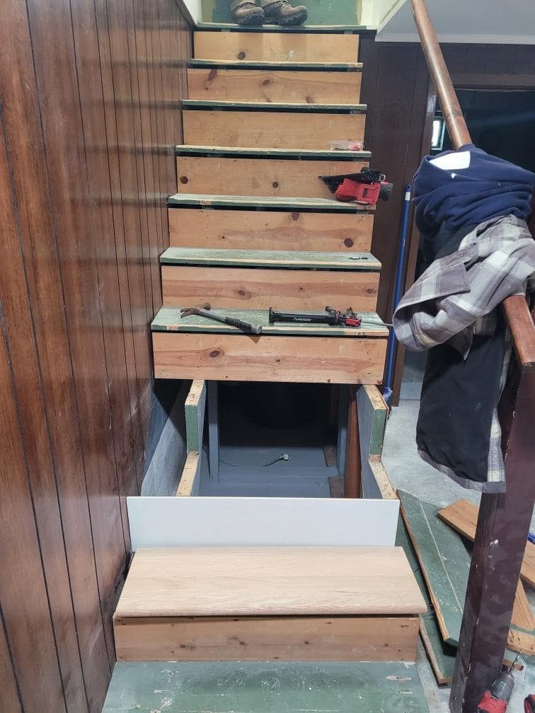 Staircase under construction. Wood steps and walls, partially enclosed; storage space visible.