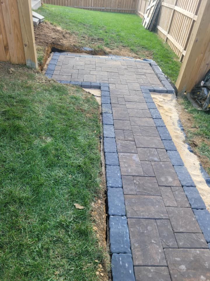 Brick pathway with dark border leading to a grassy yard, framed by wooden fences and posts.