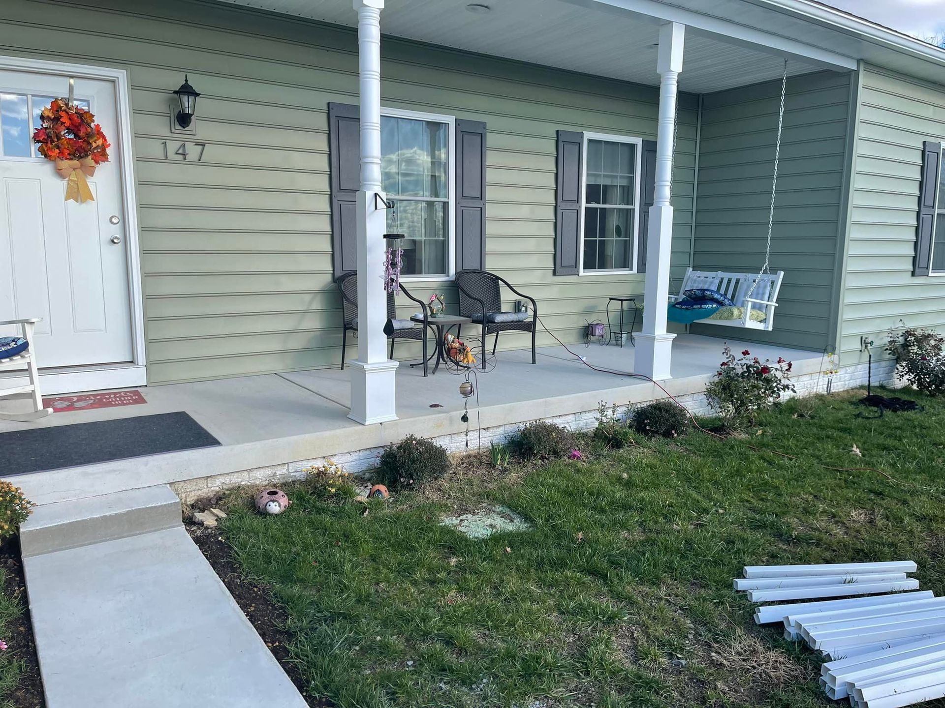 Light green house with porch, swing, and concrete path. Autumn wreath on door.