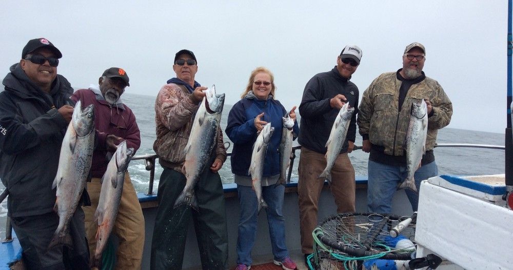 A group of people are standing on a boat holding fish.