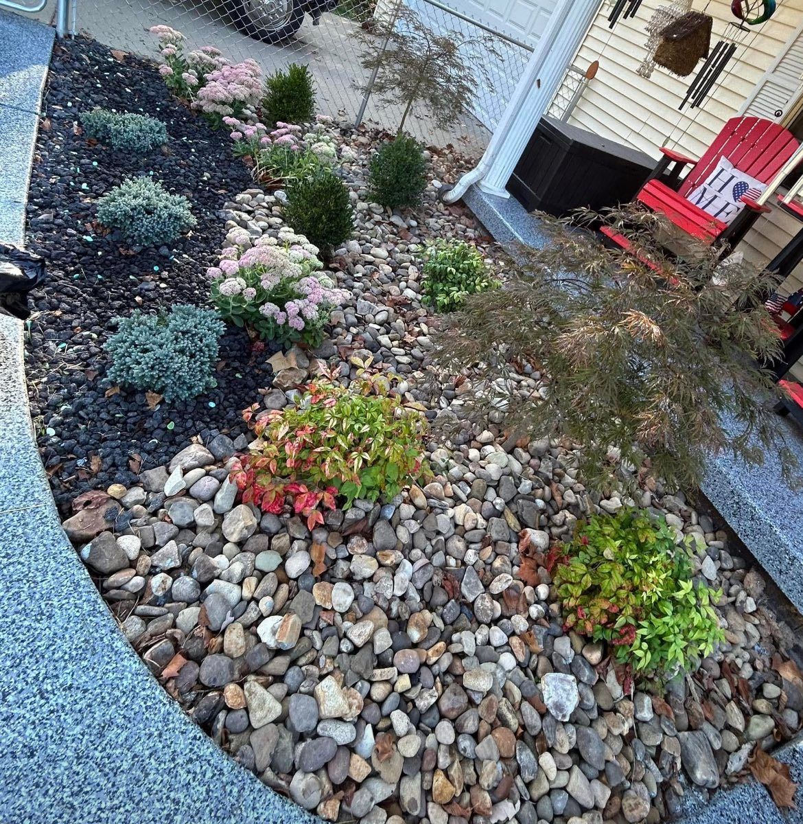 A landscaped garden bed with various plants and rocks next to a house with a red chair.