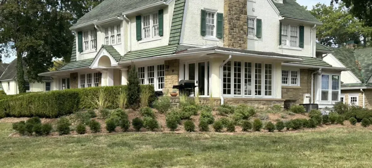 A large, two-story house with green roof and shutters, with a well-maintained lawn and landscaping.