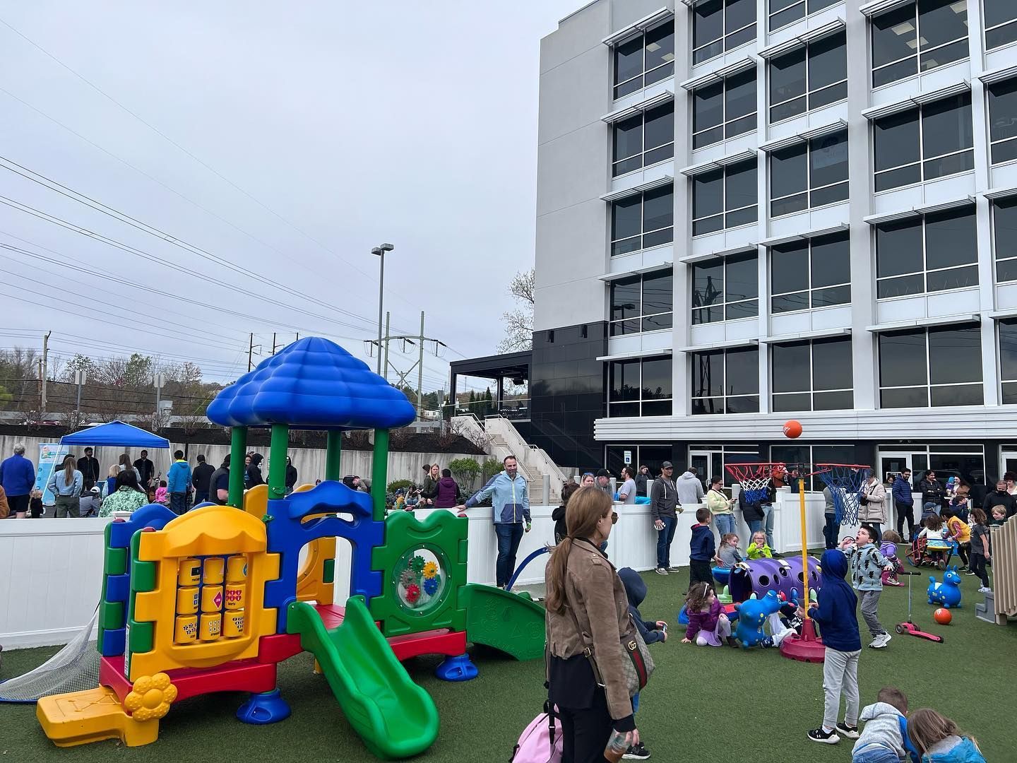 Playground with a slide, near a tall building with many windows, and people gathering.