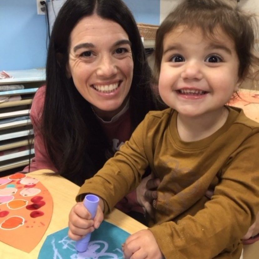 Woman and toddler smiling, working on art project at table.