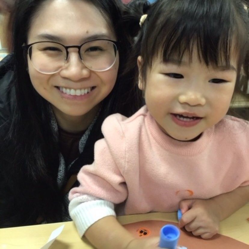 Woman with glasses smiles next to a young child in a pink sweater, both indoors.
