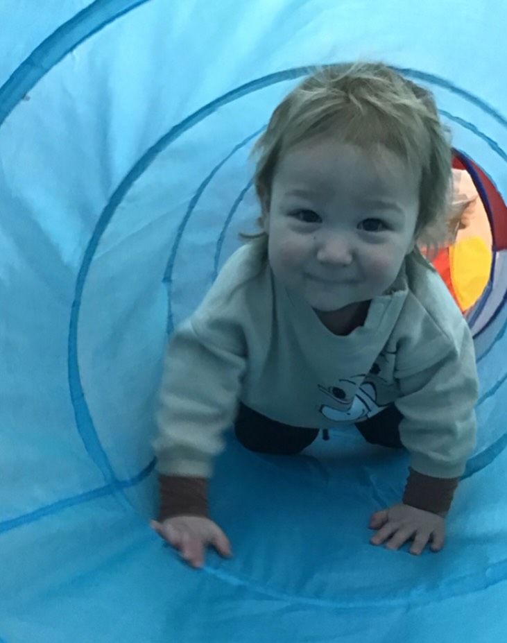 Child crawling through a blue tunnel, smiling.