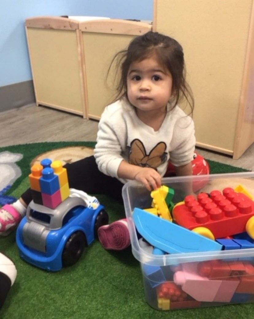 Child seated on a green mat, playing with colorful blocks and a toy car.