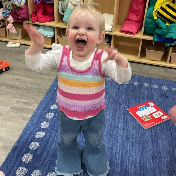 Smiling child in rainbow sweater and flared jeans, arms raised excitedly.