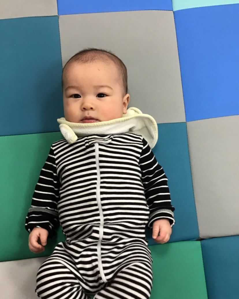 Baby in striped onesie with bib on play mat.