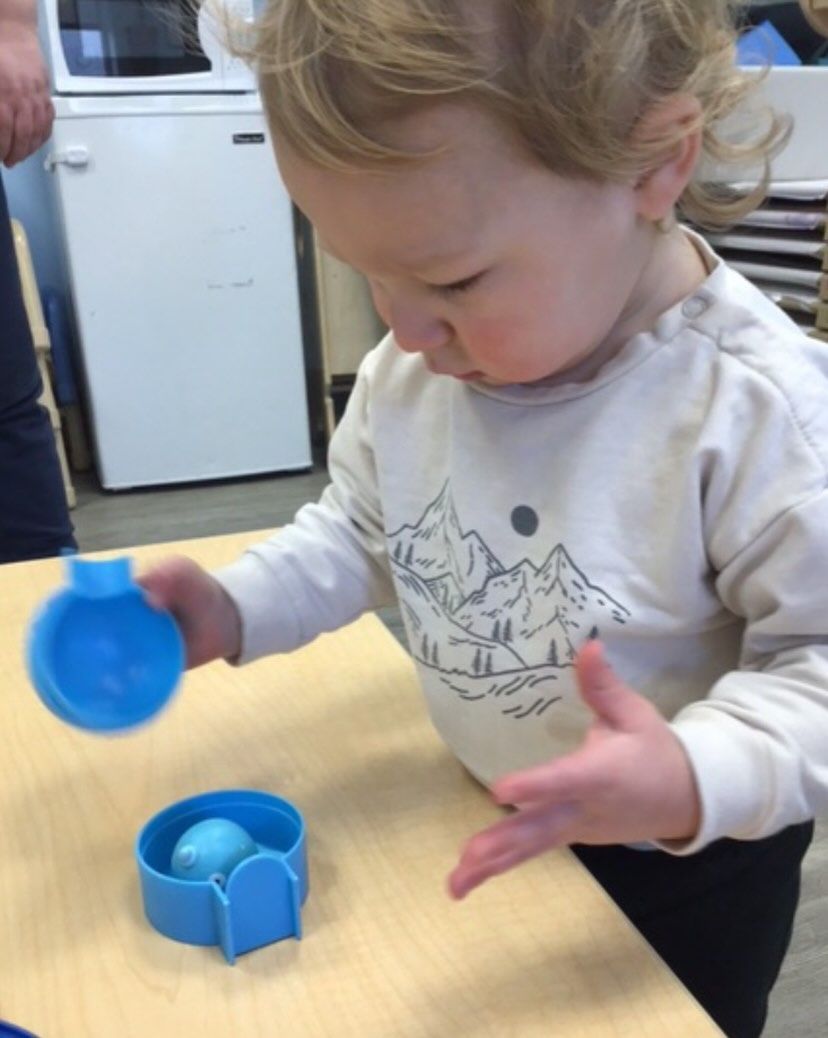 Toddler with curly hair playing with blue toy cups at a table.