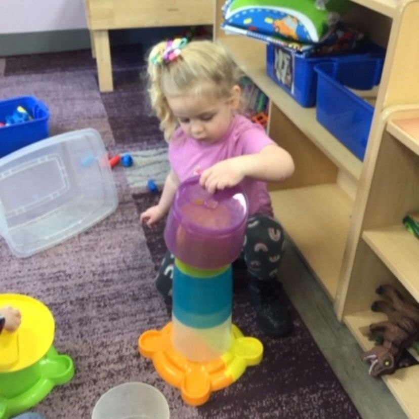Young child in pink shirt playing with a colorful toy tower indoors.