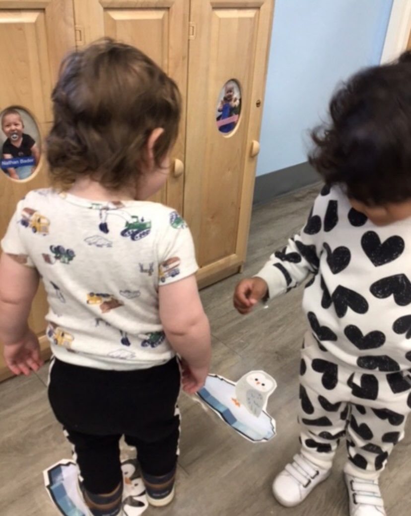 Two toddlers, one in patterned pajamas, interact indoors. A third child peers from a cabinet.