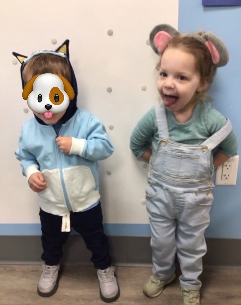 Two children in costumes: one a dog, the other a mouse. They stand against a wall, playfully posing.