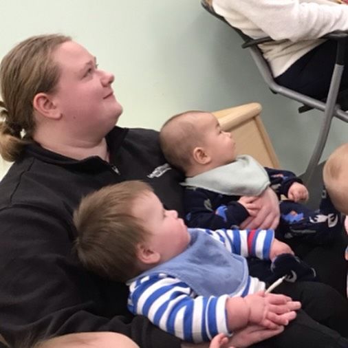 Woman holding two babies, looking up. One baby wears a bib, the other a striped shirt.