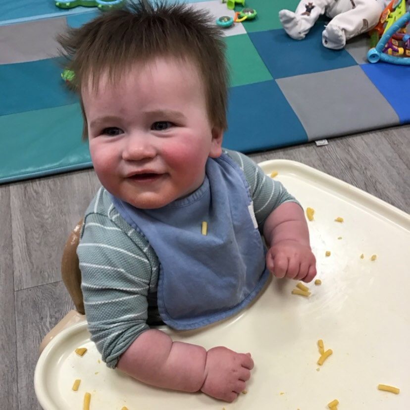 Smiling baby in high chair wearing a bib, scattered food on tray.