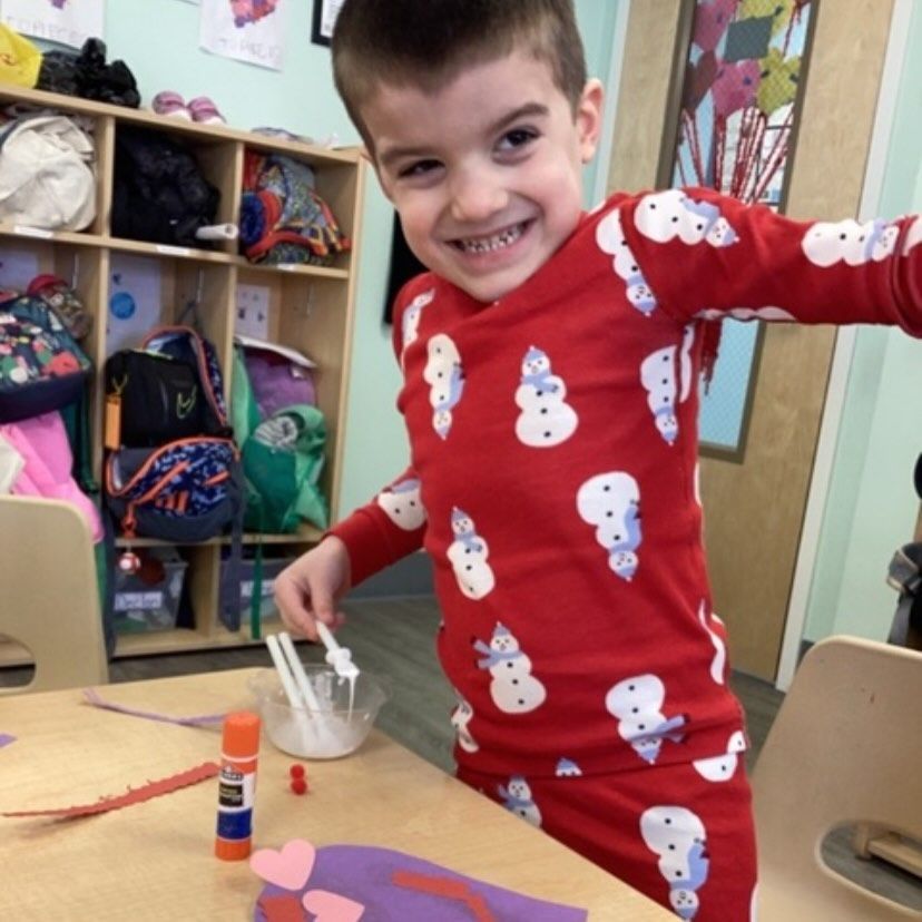 Boy in snowman pajamas smiling, crafting at a table.