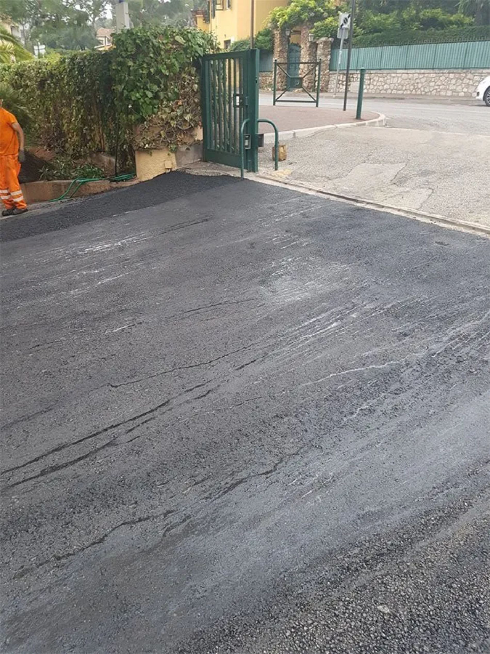 Vialetto d'accesso in asfalto appena asfaltato con un cancello verde sullo sfondo.