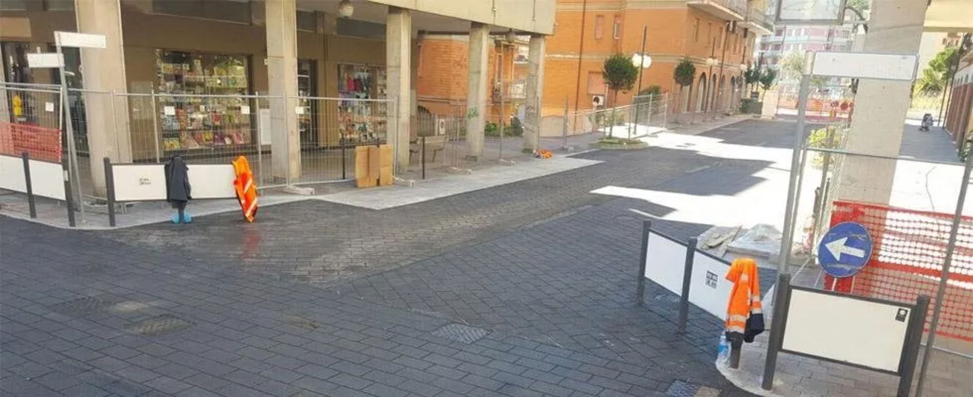 Scena di strada con operai con giubbotti arancioni, strada chiusa con cartelli.