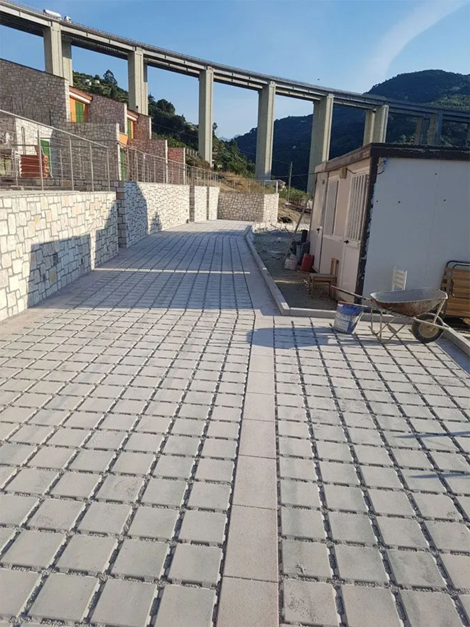 Sentiero lastricato di fronte a un edificio con un ponte alto sullo sfondo, sotto un cielo azzurro.
