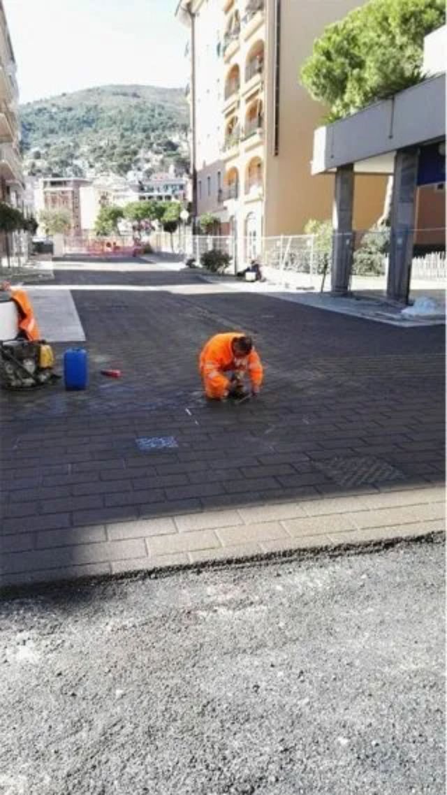 Operai in tute arancioni su una strada asfaltata buia, con le montagne sullo sfondo.