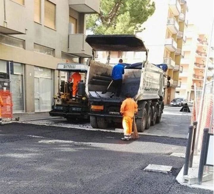 Operai stradali asfaltano una strada utilizzando un camion e macchinari.