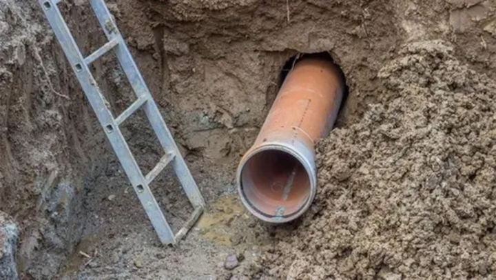 Un tubo che sporge da un buco nel terreno, con una scala nelle vicinanze.