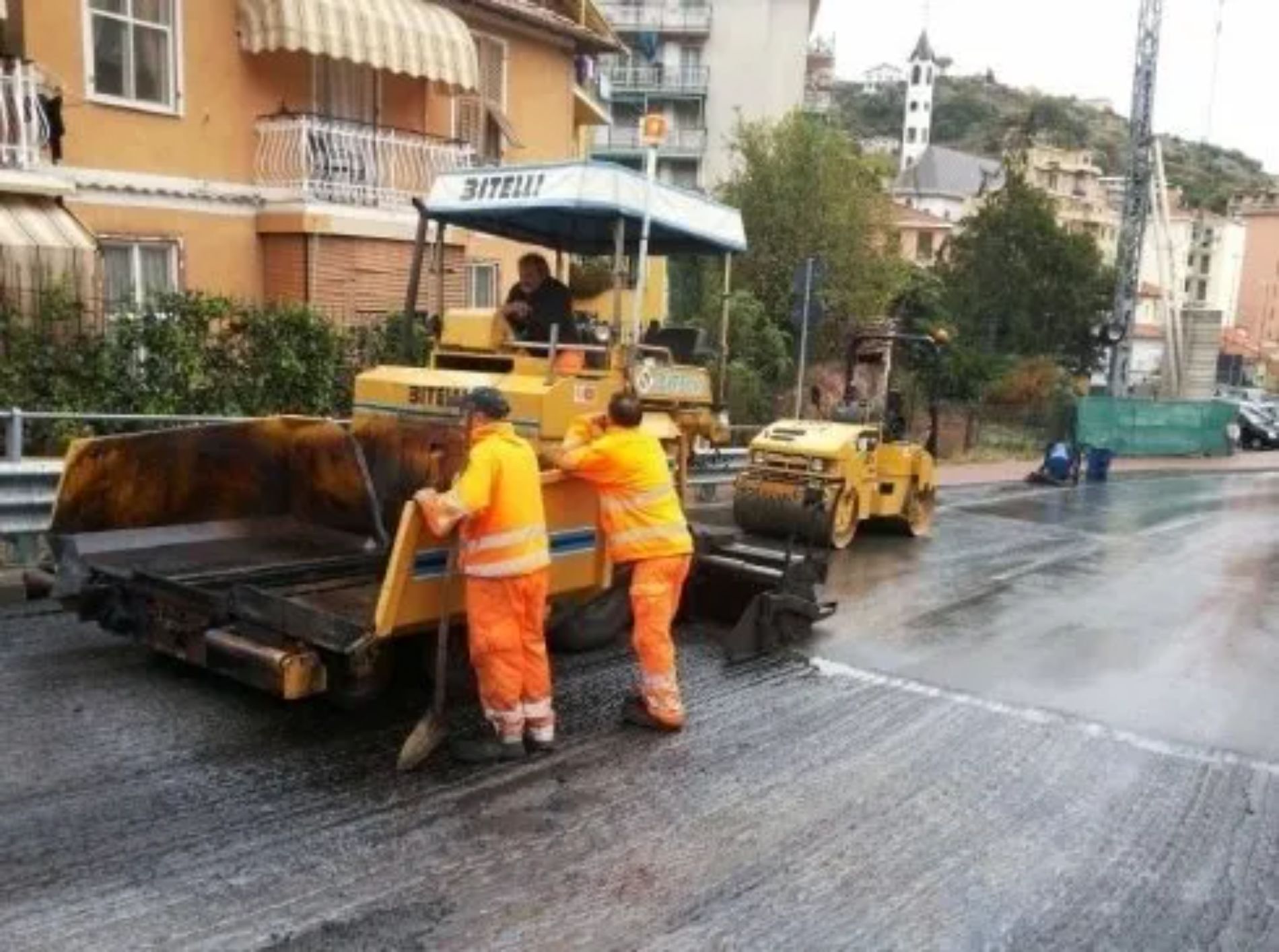 Operai stradali che asfaltano una strada con macchinari, operai con giubbotti arancioni.