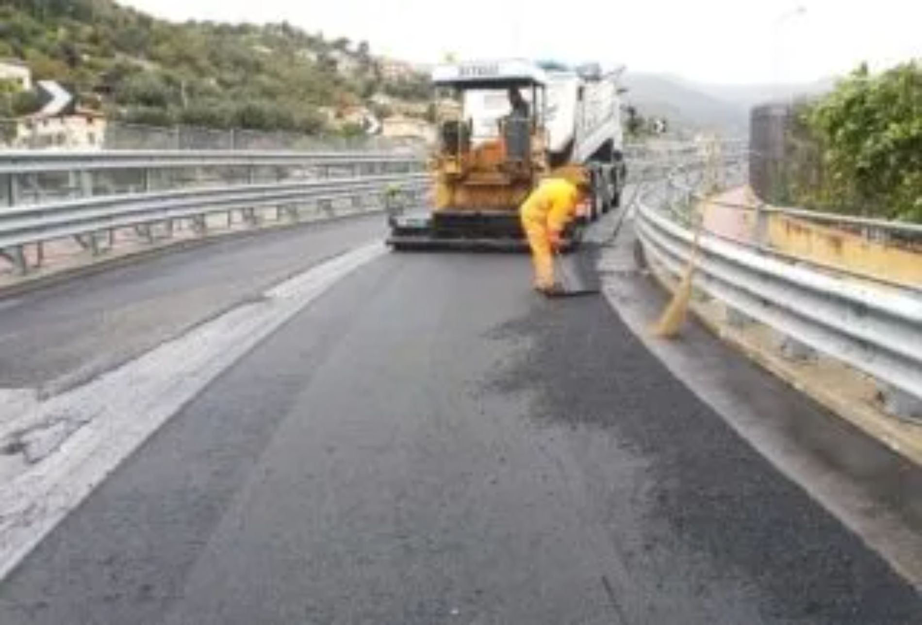 Macchina asfaltatrice sul ponte; operaio in tuta arancione.