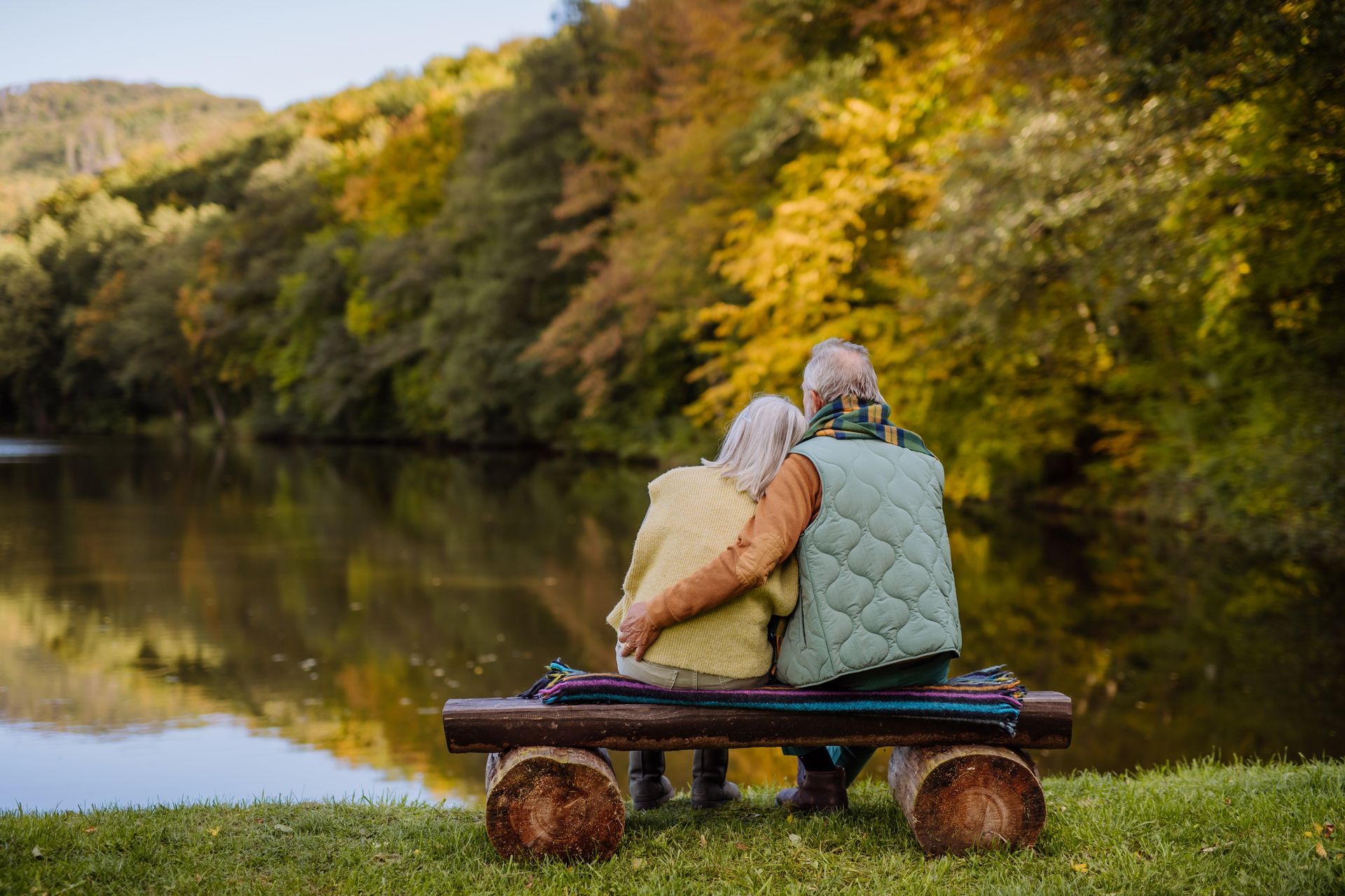 Couple embracing on a bench, overlooking a lake and fall foliage.