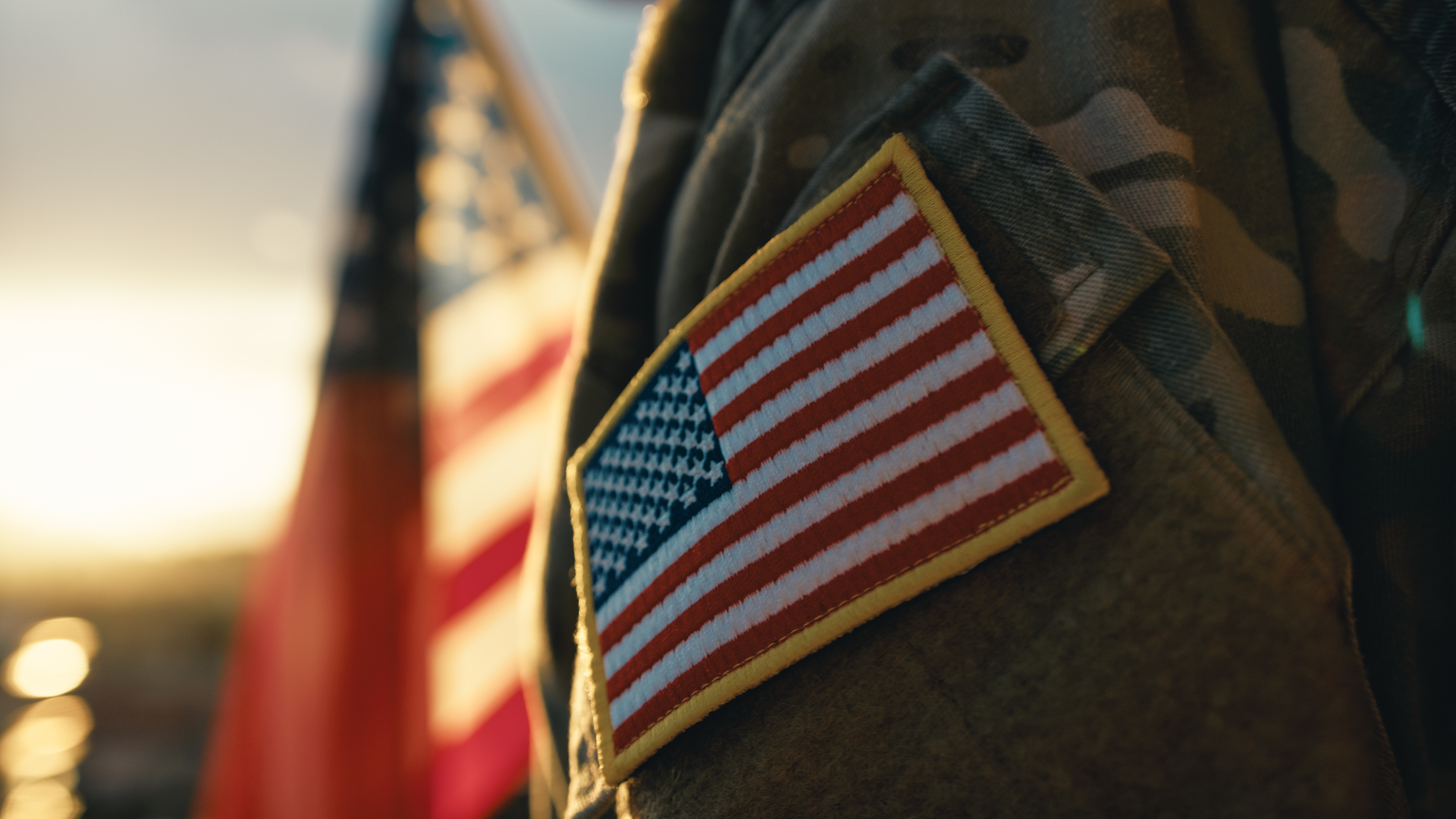 American flag patch on a military uniform with a blurred American flag background.