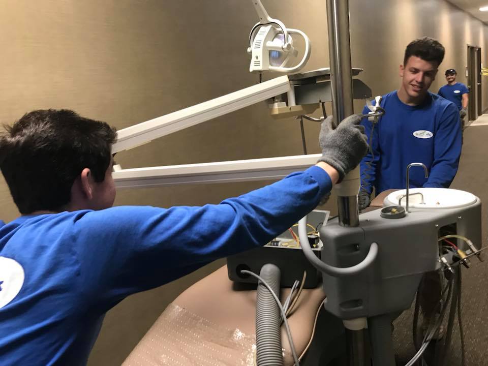 Two men in blue shirts are working on a dental equipment