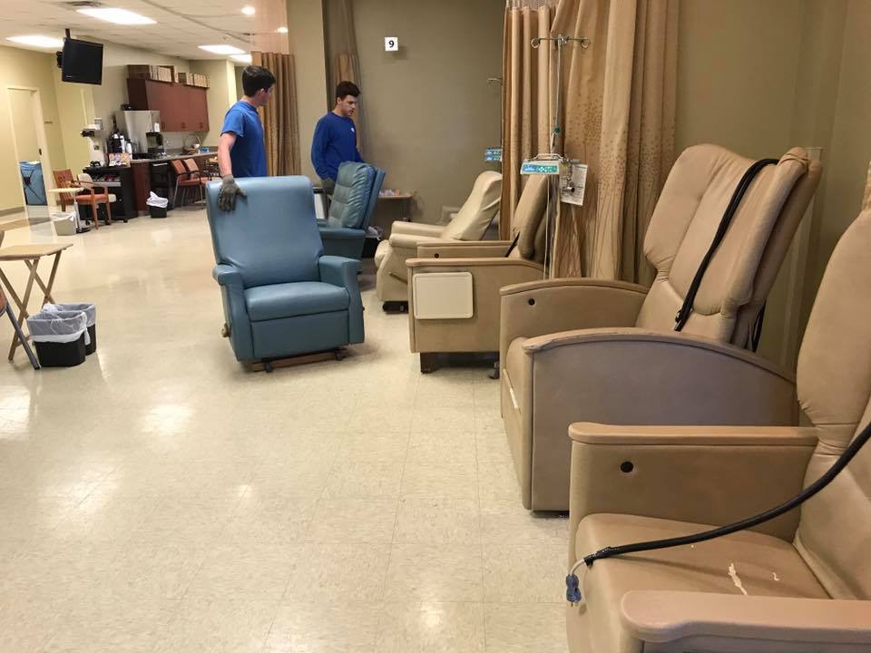 Two men are cleaning chairs in a hospital room.