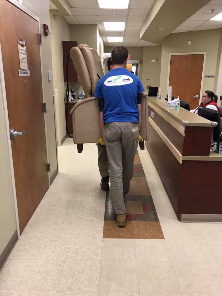 A man in a blue shirt is carrying a chair down a hallway