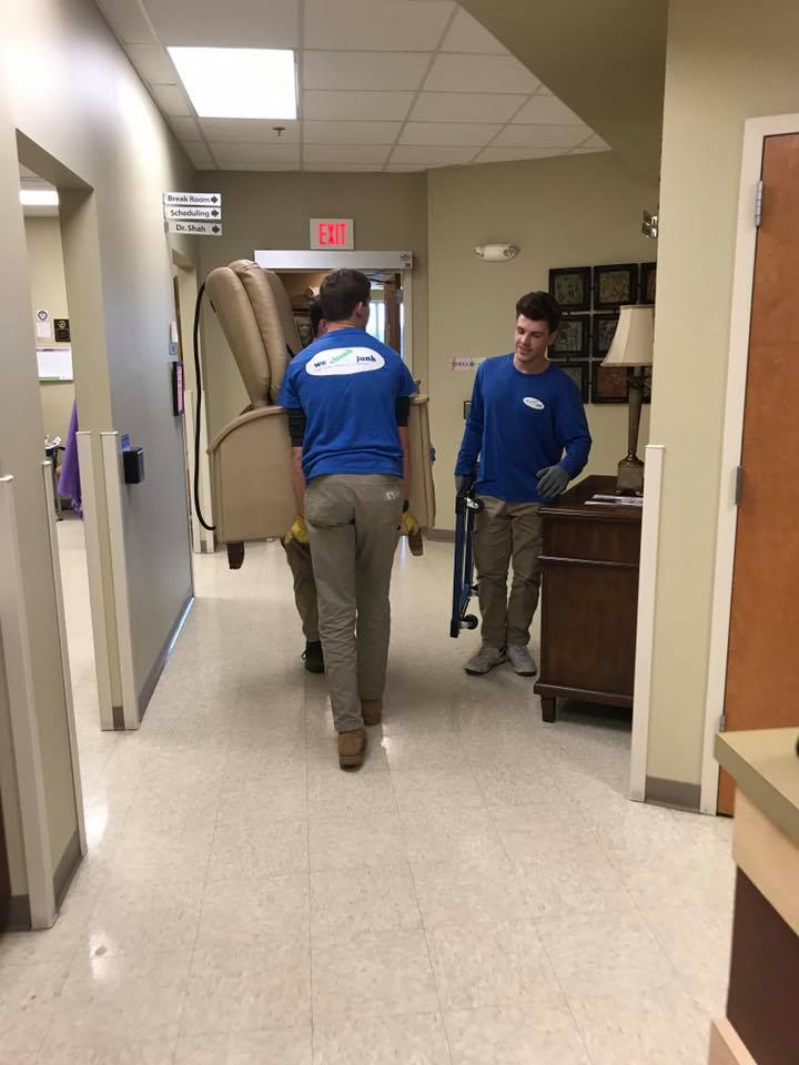 Two men are carrying a chair down a hallway.