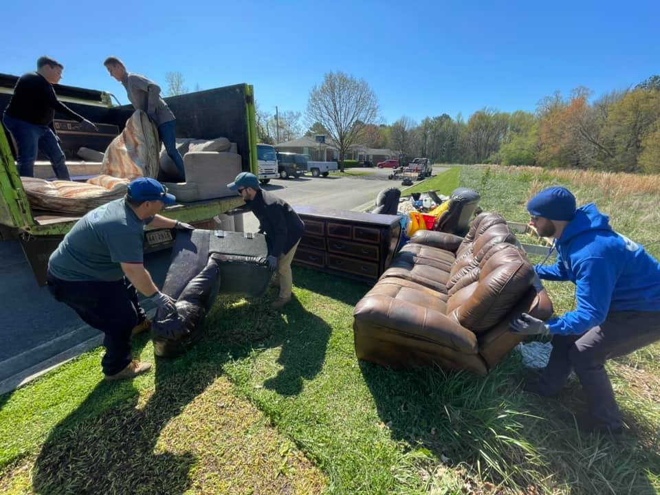 A group of people are moving a couch in a field.