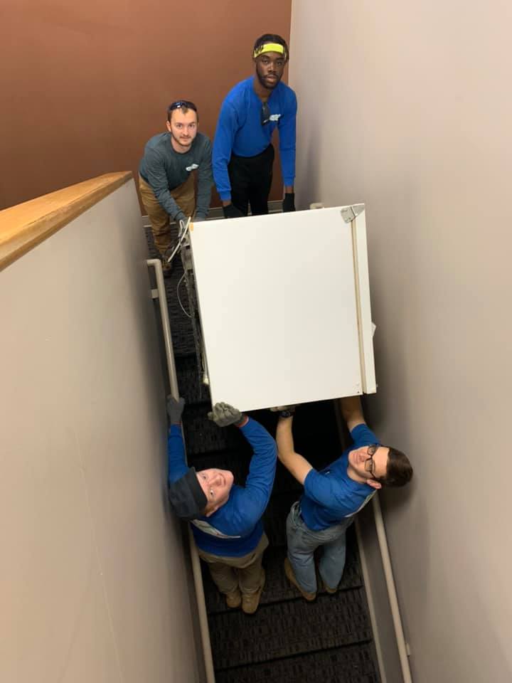 A group of men are carrying a refrigerator up a set of stairs.