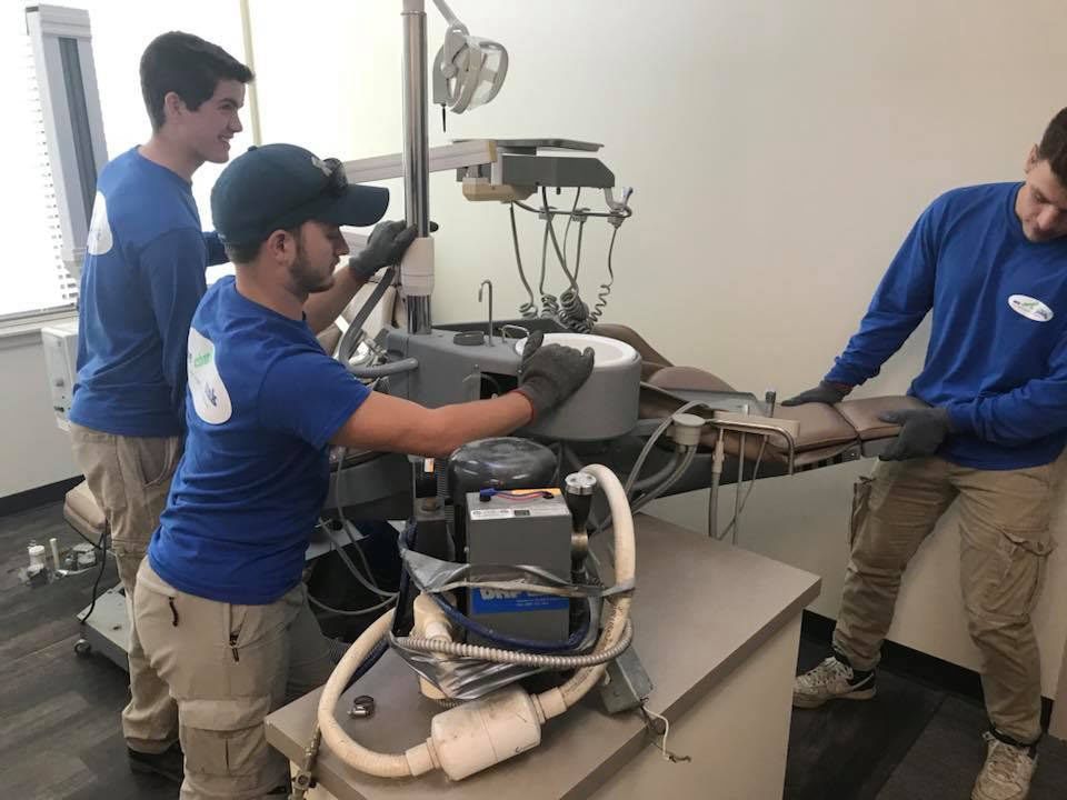 Three men are working on a dental equipment in a room.