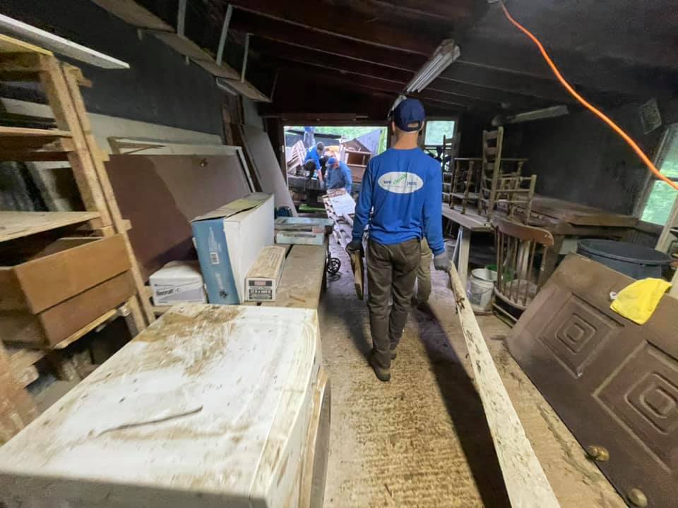 A man in a blue shirt is walking through a messy room.