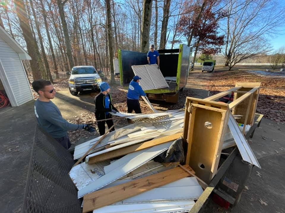 A man is standing next to a pile of junk in front of a dumpster.