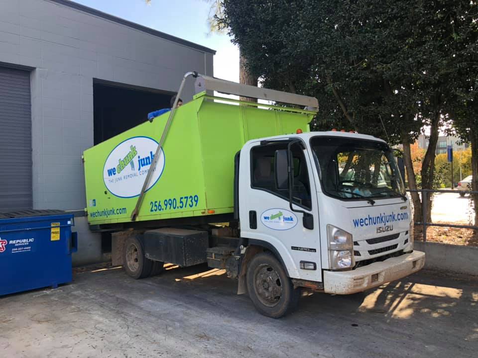 A green and white garbage truck is parked in front of a building.