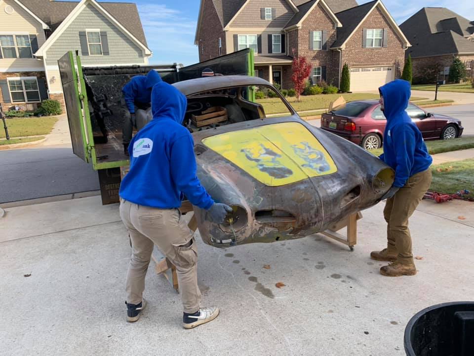 A group of people are moving a car in a driveway.