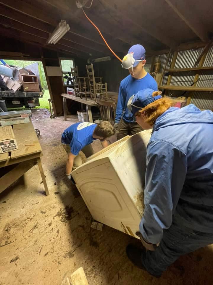 A group of people are working on a washing machine in a garage.